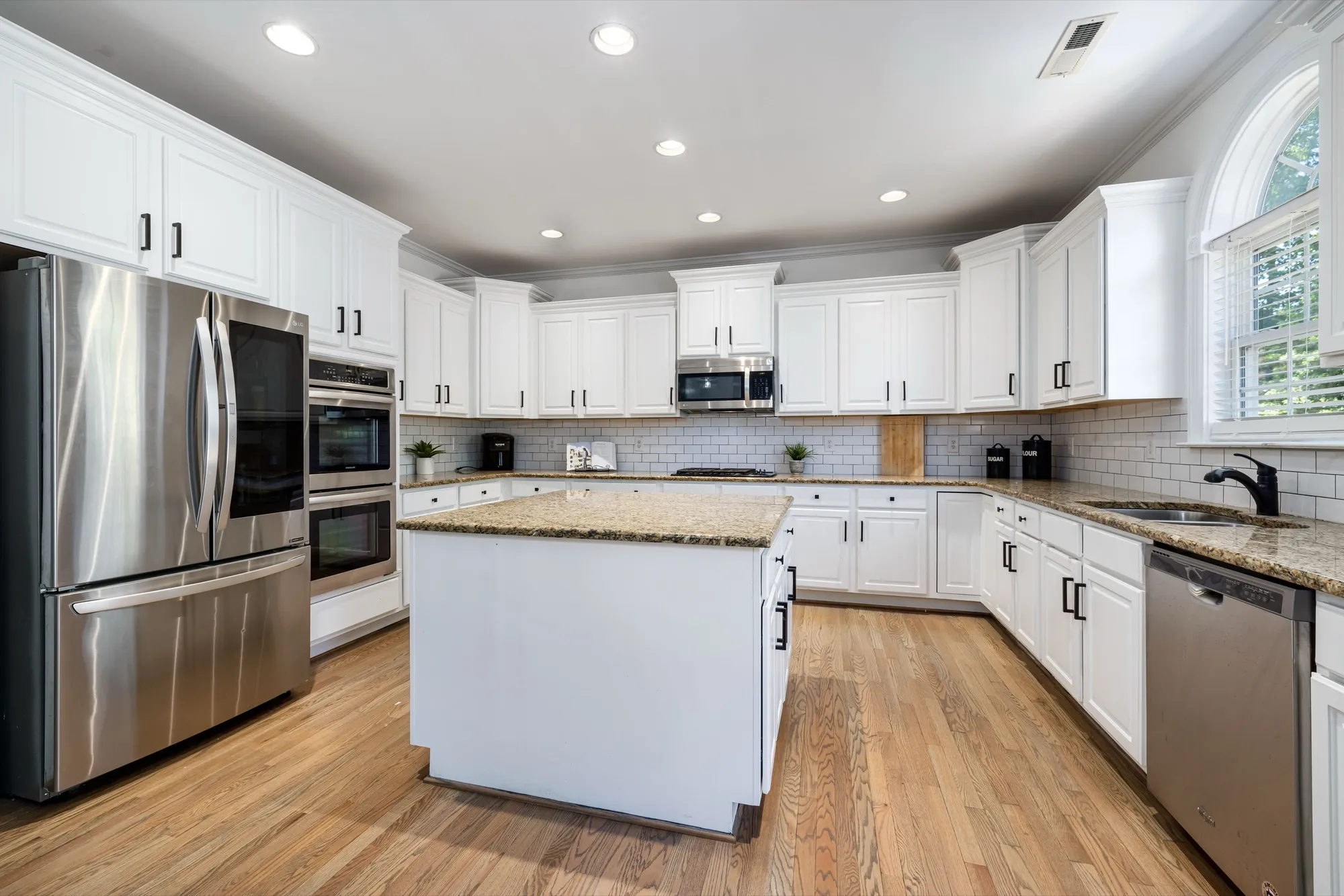 White kitchen with matte black cabinet hardware and a granite island